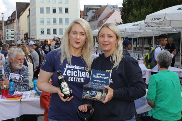 Zwei Frauen stehen an einem Marktstand und halten Produkte in den Händen.