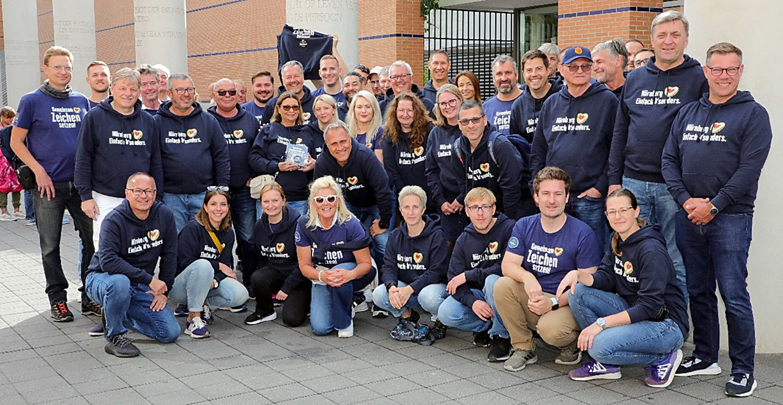 Eine Gruppe von etwa 30 Personen posiert in blauen Oberteilen für ein Gruppenfoto.