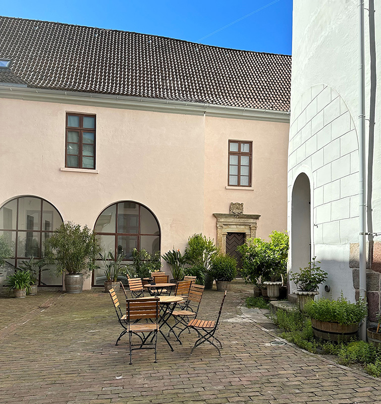 Ein Innenhof mit einer Sitzgruppe aus Tisch und Stühlen, umgeben von bepflanzten Töpfen.