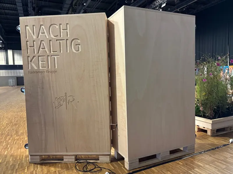 Zwei große Holzkisten stehen in einer Halle, die eine trägt den Schriftzug Nachhaltigkeit.