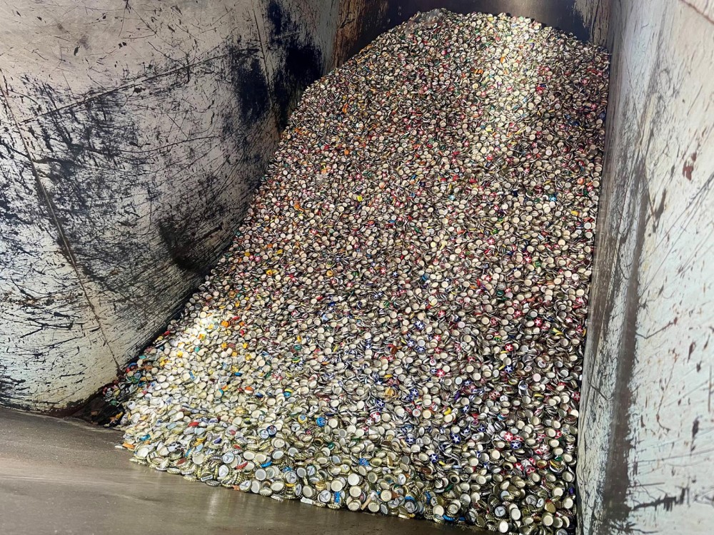 Ein großer Haufen Kronkorken liegt in einem industriellen Metallcontainer.