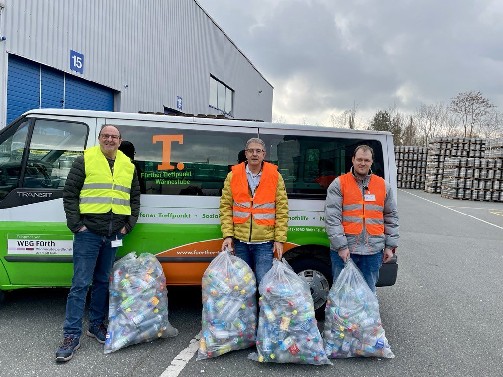 Drei Männer stehen vor einem Kleinbus, zwei halten große Säcke mit Pfandflaschen.